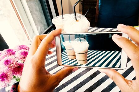 Hand holding mobile and taking photo of iced coffee in the cafe