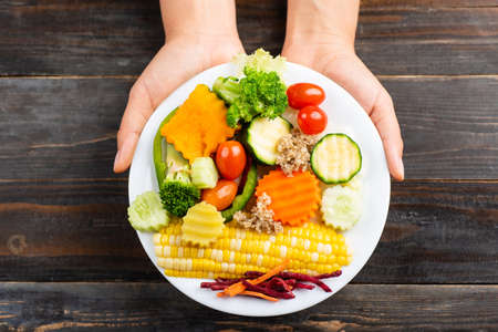 Vegetables salad on white dish holding by hand on wooden background, top viewの写真素材