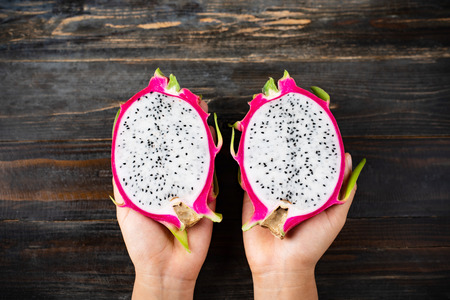 Half dragon fruit holding by hand on wooden background, top view, tropical fruitの写真素材