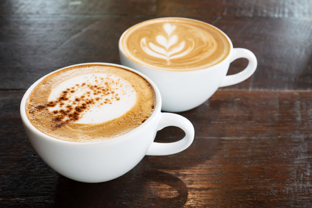 Cup of hot cappuccino and latte art coffee on wooden table in the coffee shopの写真素材