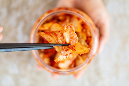 Kimchi cabbage in a bowl holding by hand with chopsticks for eating, Korean food, top viewの写真素材