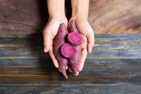 Purple sweet potatoes holding by hand on wooden backgroundの写真素材
