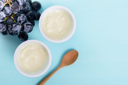 Two plastic cups of yoghurt with wooden spoon and grape on pastel background, healthy eating, top viewの写真素材