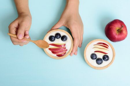 Hand holding spoon for eating yoghurt with apple and grape in a bowl  on pastel background, healthy...
