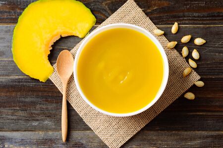 Pumpkin soup in a bowl with spoon on wooden background, top viewの写真素材