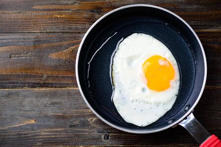 Fried egg in cooking pan on wooden background, top view