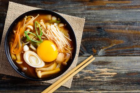 Kimchi soup with mushroom and egg yolk in a bowl and chopsticks on wooden background, Korean food, top viewの写真素材