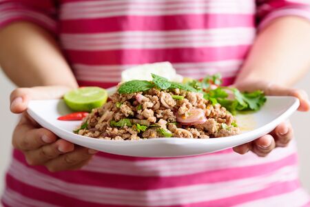 Thai food, spicy minced pork salad (Larb Moo) holding by handの写真素材