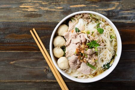 Rice noodles soup with pork and meat ball in a bowl with chopsticks on wooden table, Asian food,...