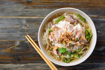 Rice noodles soup with beef in a bowl with chopsticks on wooden background, Asian food, Thai style,...