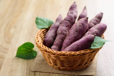 Raw purple sweet potatoes in basket on wooden tableの写真素材