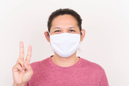 Portrait of Asian man wearing white fabric mask to protection corona virus outbreak  and showing v signの写真素材