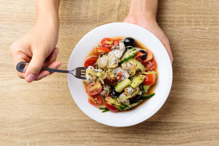 Spicy fruits and vegetables salad on white plate holding by hand and eating, Healthy food