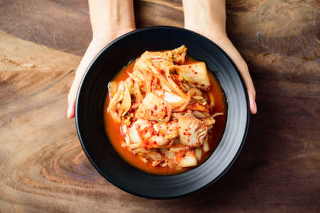 Kimchi cabbage on plate holding by hand on wooden background, Korean foodの写真素材