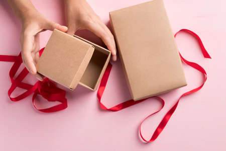 Paper gift box with red ribbon open by hand on pink background, Present for giving in special day,...