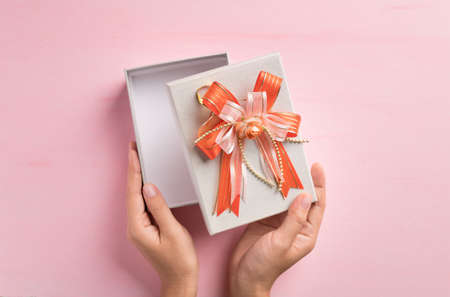 Silver gift box with orange ribbon open by hand on pink background, Present for giving in special day, Top viewの写真素材