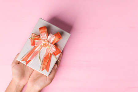 Gift box with orange ribbon holding by hand on pink background, present for giving in special day,...