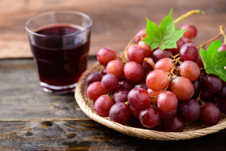 Fresh red grapes fruit in a basket and juice on wooden backgroundの写真素材