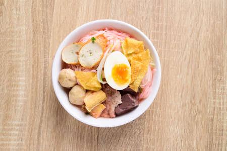Thai food (Yen Ta Fo), Rice noodles soup with red sauce and fish tofu, pork ball and fried wonton in a bowl on wooden background, Top viewの写真素材