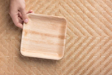 Hand holding Betel palm leaf plate (Biodegradable, Compostable or Eco friendly disposable plate) on woven bamboo sheet, sustainable conceptの写真素材
