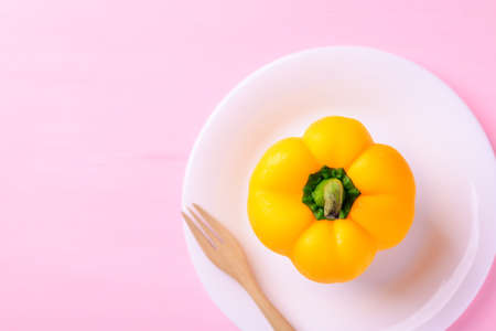 Yellow bell pepper on white plate with wooden fork on pink background, Top view