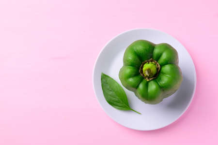 Green bell pepper with leaf on white plate with pink background, Top viewの写真素材