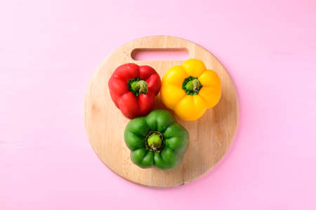 Yellow, red and green bell peppers on wooden cutting board with pink background, Top viewの写真素材