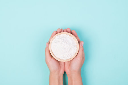 Wheat flour in a wooden bowl holding by woman hand on color background, Top viewの写真素材