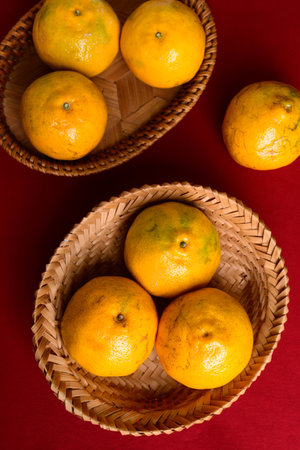 Tangerine orange fruit in bamboo basket on red background, Top viewの写真素材