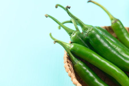 Fresh green chili peppers in a basket on green color backgroundの写真素材