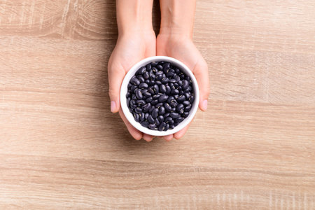 Black kidney beans in a bowl holding by hand on wooden background, Top viewの写真素材