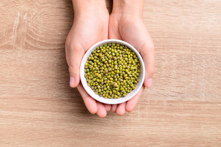 Mung beans in a bowl holding by hand on wooden background, Top viewの写真素材