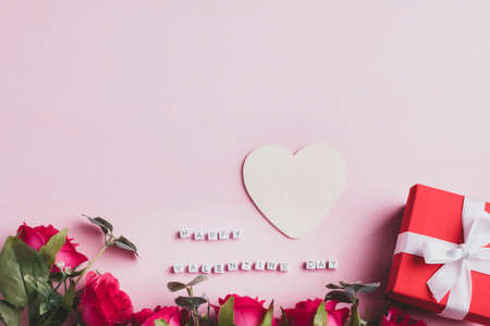 Beautiful red rose flower bouquet with gift box and happy valentine day alphabet with heart shape on pink backgroundの写真素材