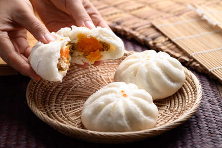 Steamed buns stuffed with minced pork and salted egg holding by hand and eating, Asian foodの写真素材