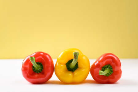 Fresh red and yellow bell peppers on white and yellow backgroundの写真素材