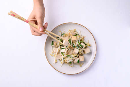 Stir fried tofu with mung bean sprouts eating by using chopsticks on white background, Asian healthy...