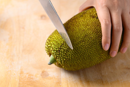 Hand holding young jackfruit and cutting by kitchen knife on wooden board, Food ingredient in...