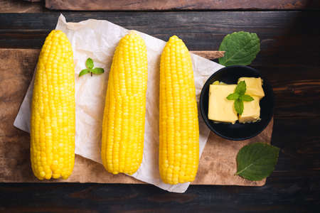 Sweet corn cob and butter in a bowl on wooden background, Top view