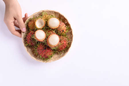 Ripe rambutan fruit in a bamboo basket holding by woman hand on white background, Rambutan is tropical fruit and native Southeast Asia, juicy and sweet tasteの写真素材