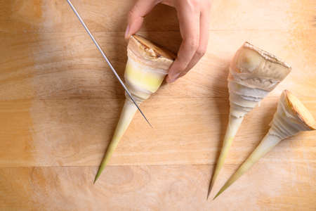 Hand holding kitchen knife and chopping peeled bamboo shoot on wooden board, Edible vegetable in Asian cuisineの写真素材