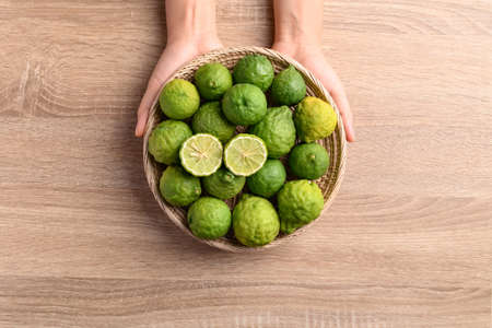 Fresh bergamot fruit in a basket holding by woman hand on wooden background, Food ingredients and extract used for medicine, tea, perfumes and cosmeticsの写真素材