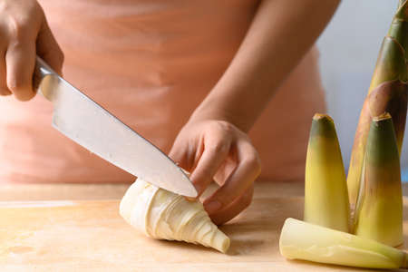 Hand holding kitchen knife and chopping peeled bamboo shoot on wooden board, Edible vegetable in Asian cuisineの写真素材