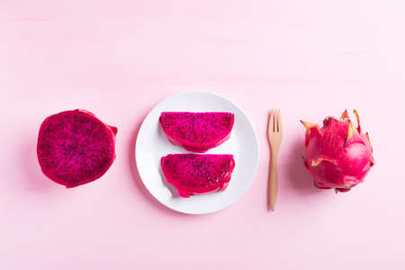 Sliced red dragon fruit or pitaya on white dish with wooden fork ready to eating on pink background,...