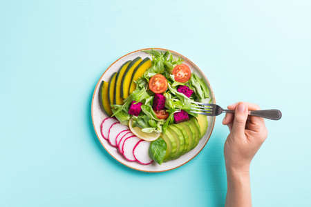 Vegan salad fruits and vegetables dish with avocado, dragon fruit, radish, pumpkin, tomato, corn...