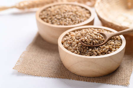 Wheat grain in a wooden bowl with spoon on white background