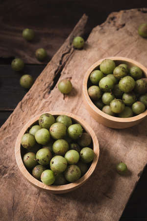 Wild Indian gooseberry or amla in a bowl on wooden background, Fruit tree in Asia use in various...