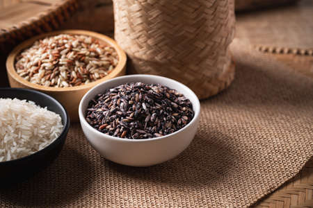 Various Organic Thai rice grain (purple, white and brown rice) in a bowl on brown background