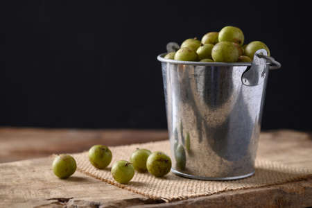 Wild Indian gooseberry or amla in a silver bucket on wooden with black background, Fruit tree in...