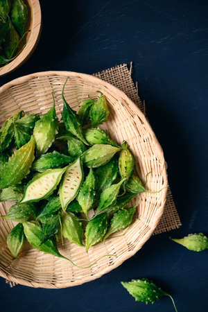 Fresh Organic bitter gourd or bitter melon in a bamboo basket on dark background, Food ingredients...
