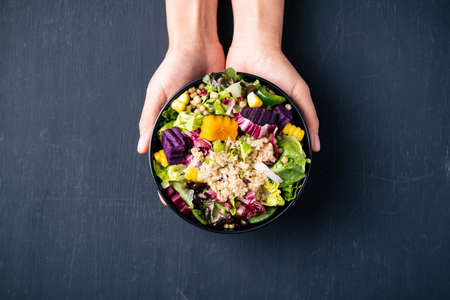 Fresh organic vegetables salad with quinoa seed in bowl holding by hand on black background, Healthy Vegan food, Top viewの写真素材